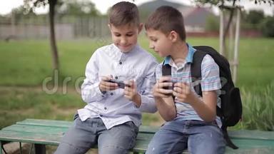 两个男孩坐在长凳上玩网络<strong>游戏</strong>。 一个带<strong>背包</strong>的男孩。 年轻人用电话